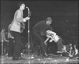 The Beatles onstage during Beatlemania: fans throw themselves at their idols, here one is being held back by Beatles roadie, Mal Evans.